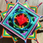 Mandala artesanal de forma cuadrada tejido con hilos multicolores en capas geométricas.