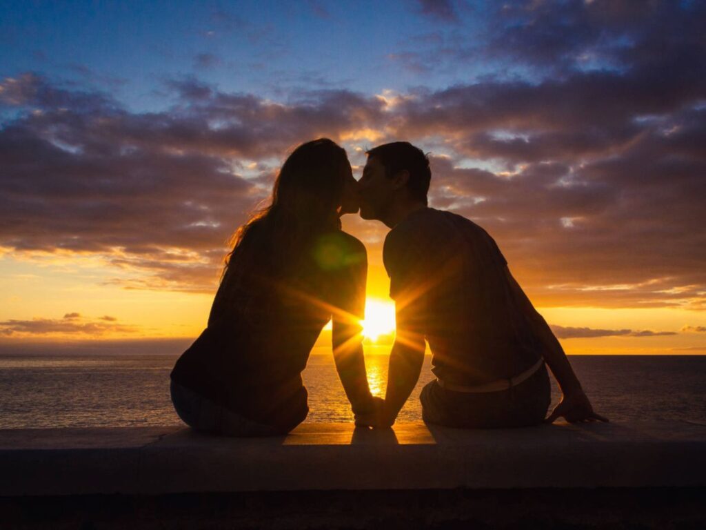 Pareja besándose al atardecer frente al mar, simbolizando amor, conexión emocional y presencia compartida.